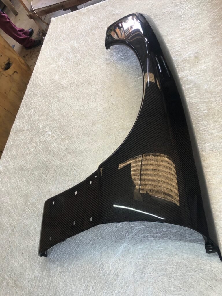 a pre-made custom carbon fiber fender, featuring a sleek and glossy finish with pre-drilled mounting holes. 