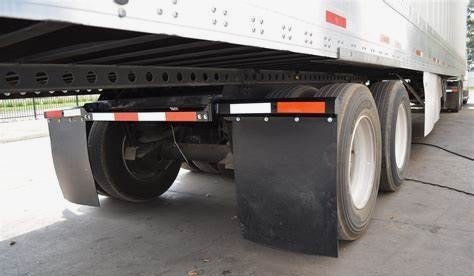 Semi-trailer with tandem axle equipped with large black mud flaps, designed to reduce road spray and protect other vehicles from debris