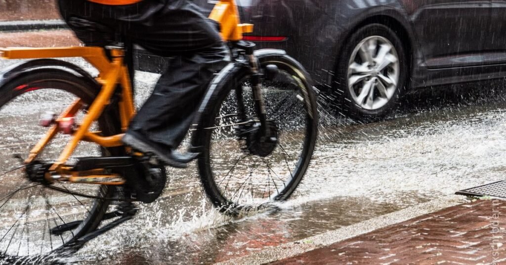 A cyclist riding through rain demonstrates how bike fenders can prevent water from splashing onto the rider, keeping them dry and comfortable during wet weather commutes.