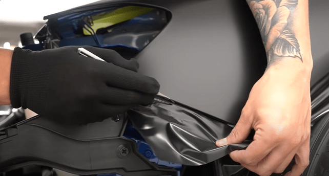 A close-up shot of a person wearing gloves applying a matte black vinyl wrap to a Jeep fender