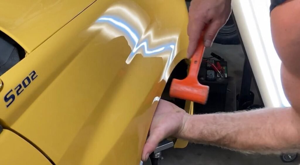 Using a rubber mallet to carefully reshape a car's fender during the unrolling process