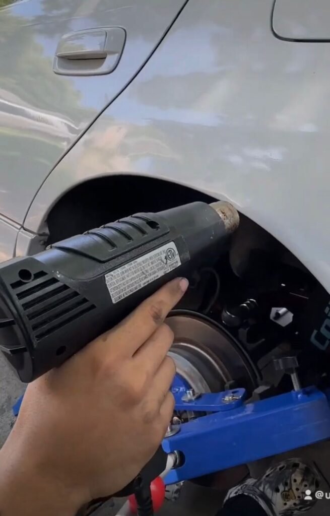 Person using a heat gun on a car fender to soften the paint before unrolling.